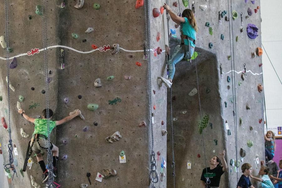 三名青少年大学生在健保中心室内攀岩墙上攀爬
